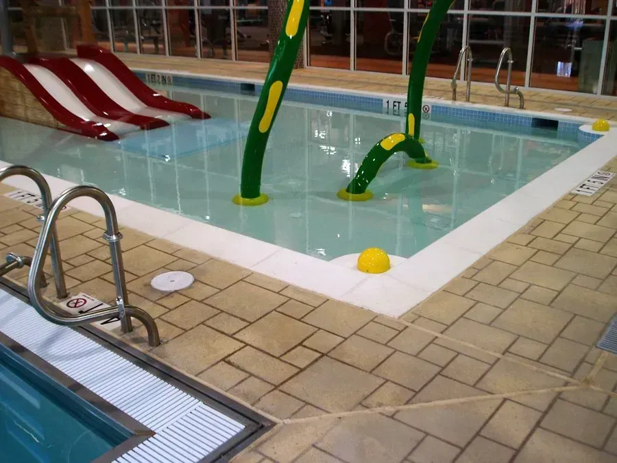 Indoor shallow pool with waterslides and water features. Red and white slides. Green and yellow water spouts.