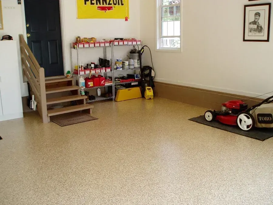 Garage with speckled flooring, stairs, shelving with tools, and a lawnmower.