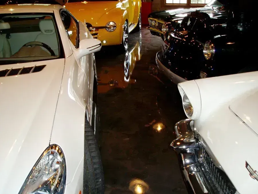 Cars of various colors parked in a garage with a reflective floor.