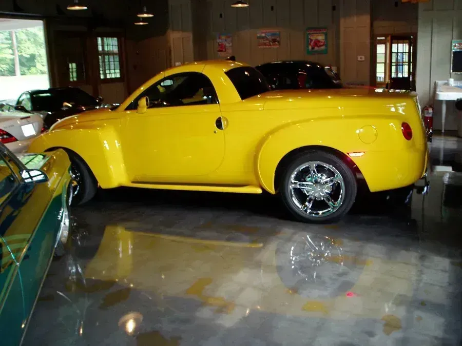 Yellow Chevrolet SSR truck with chrome wheels in a garage.