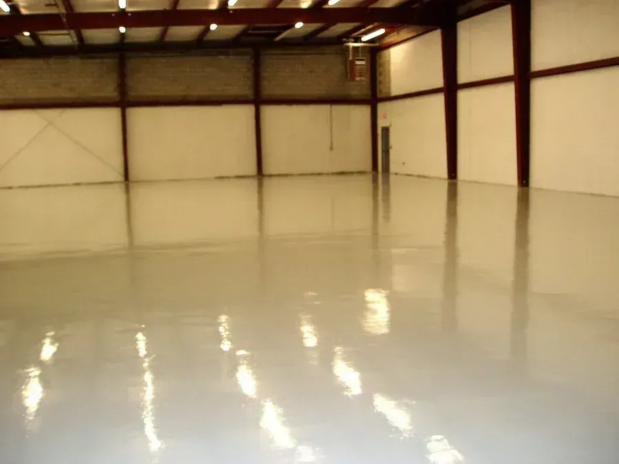 Empty industrial warehouse with shiny, light-gray epoxy floor and white walls.