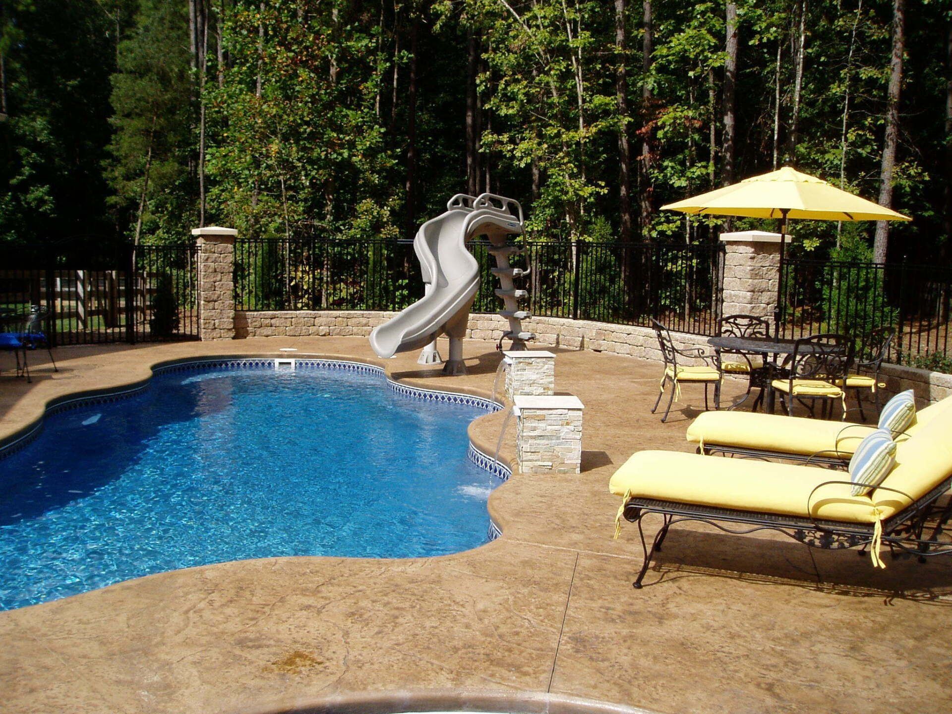Poolside scene with a pool, slide, patio furniture, and yellow umbrella.