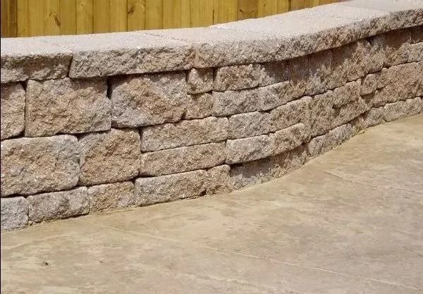 Curved retaining wall made of light brown stone blocks, built on a concrete surface.