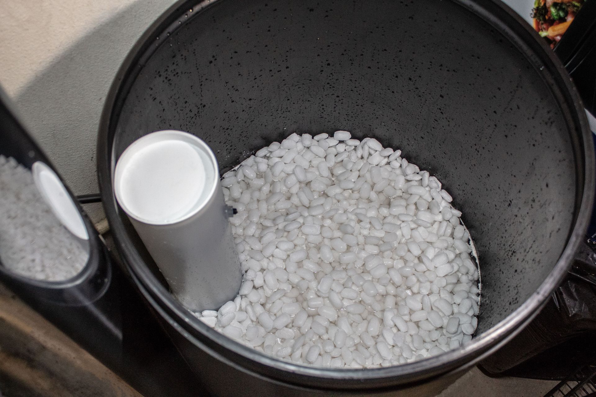 Inside a black trash can, a white cylinder stands amidst white pebbles.