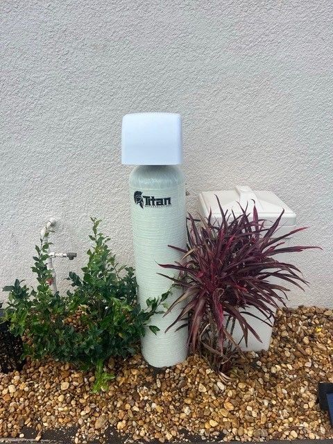 Water softener and salt container outside, with plants and gravel.