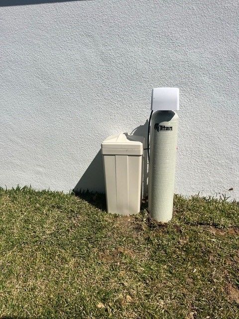 Water softener system next to a stucco wall, standing on grass.
