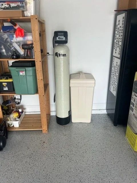 Water softener and salt container in a garage, next to a shelf and a black cabinet.