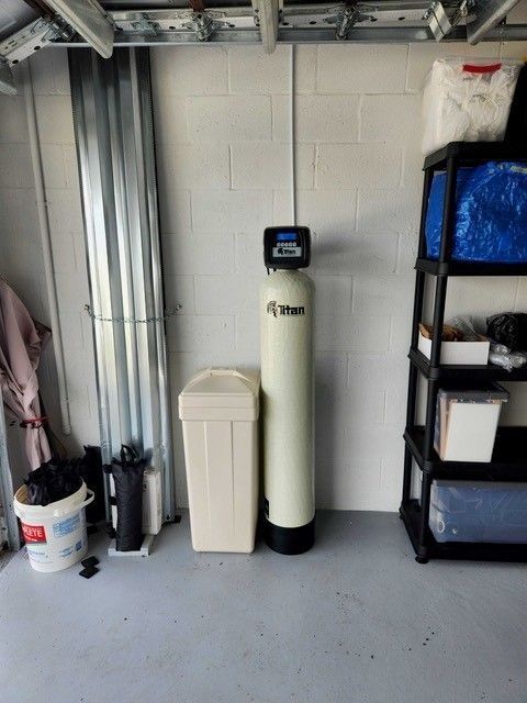 A water filtration system in a garage setting with storage shelves and a trash can.