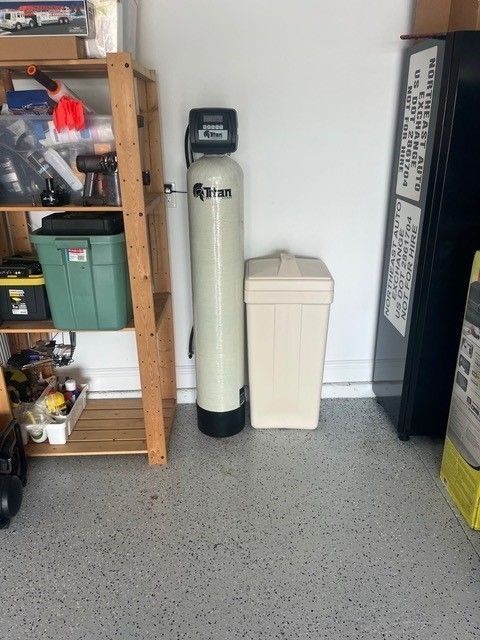 Water softener next to salt tank in a garage. Shelf with items on the left.