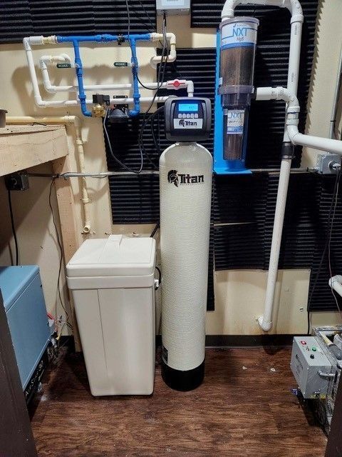 Water filtration and softening system in a room with pipes, tanks, and a digital display.