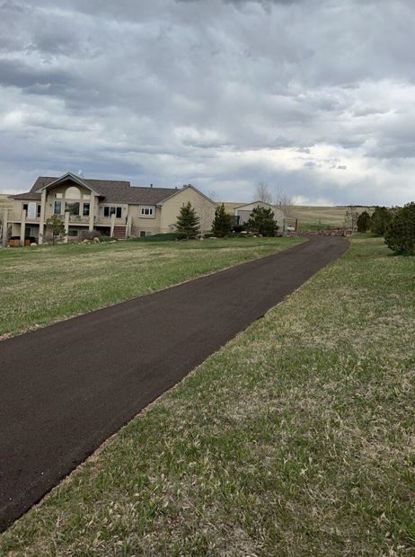 A road going through a grassy field with a large house in the background