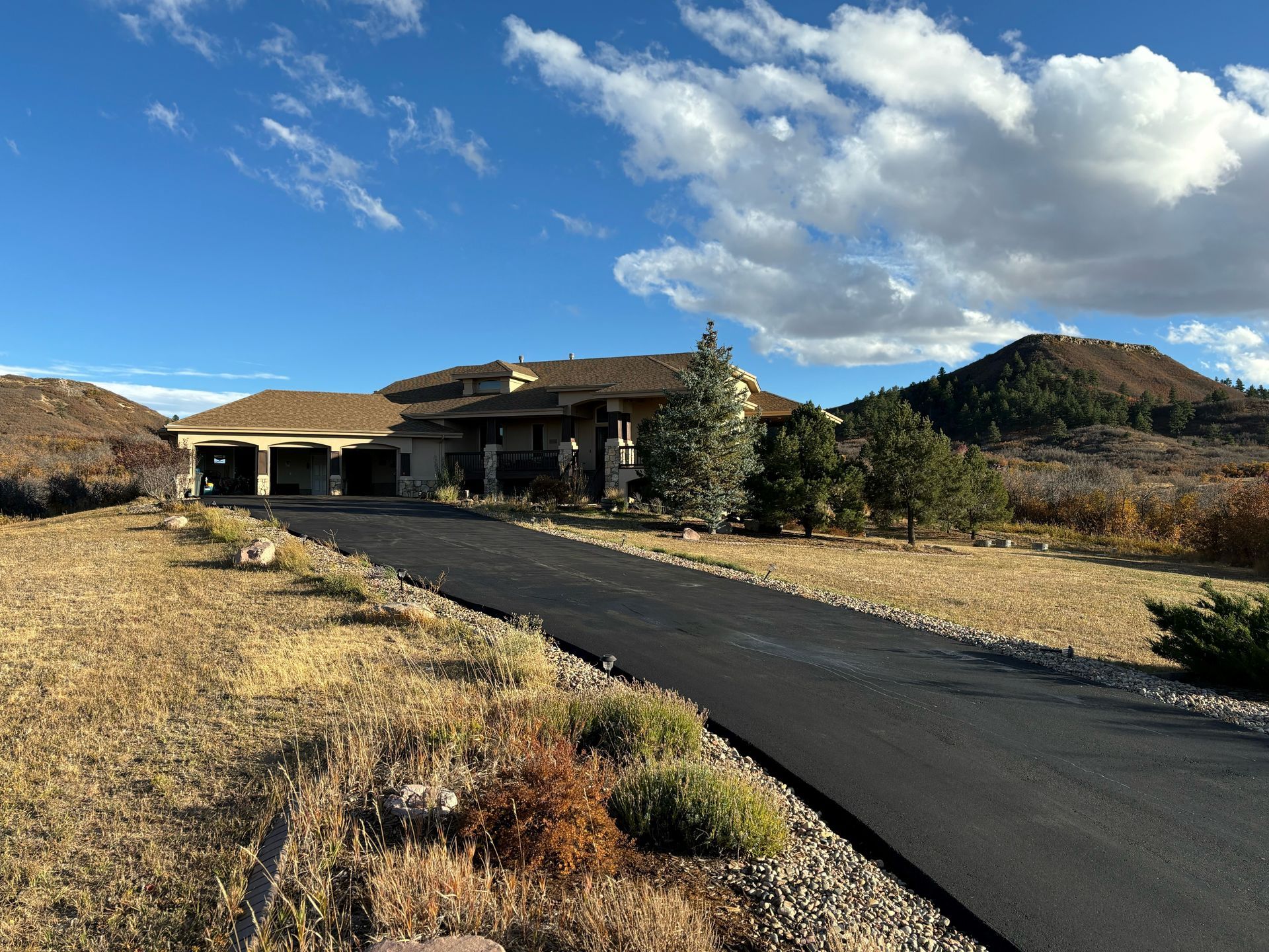 An asphalt driveway leads to a big house.