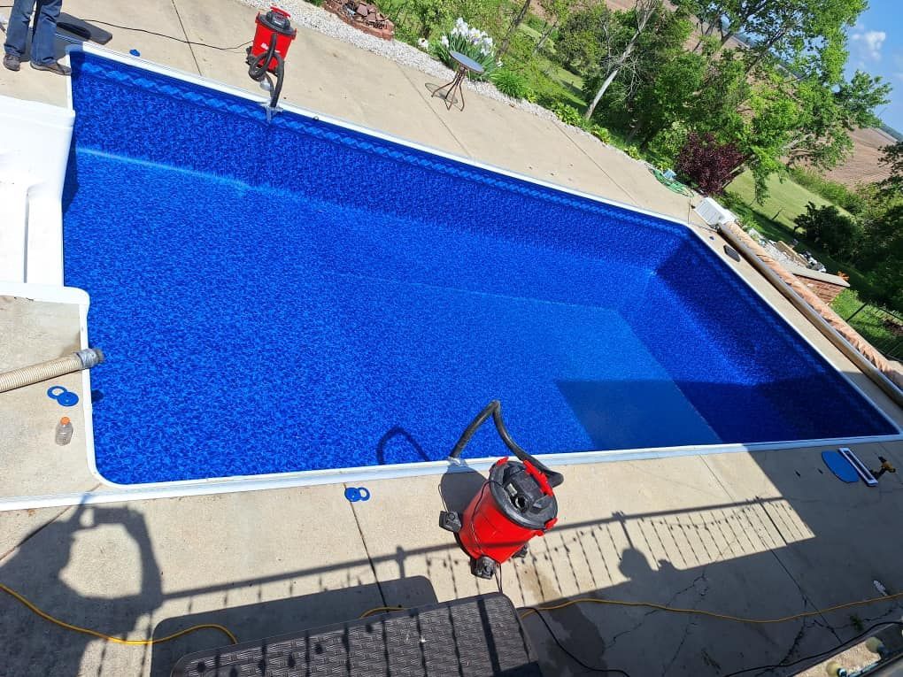 A large blue swimming pool with a red vacuum cleaner in front of it