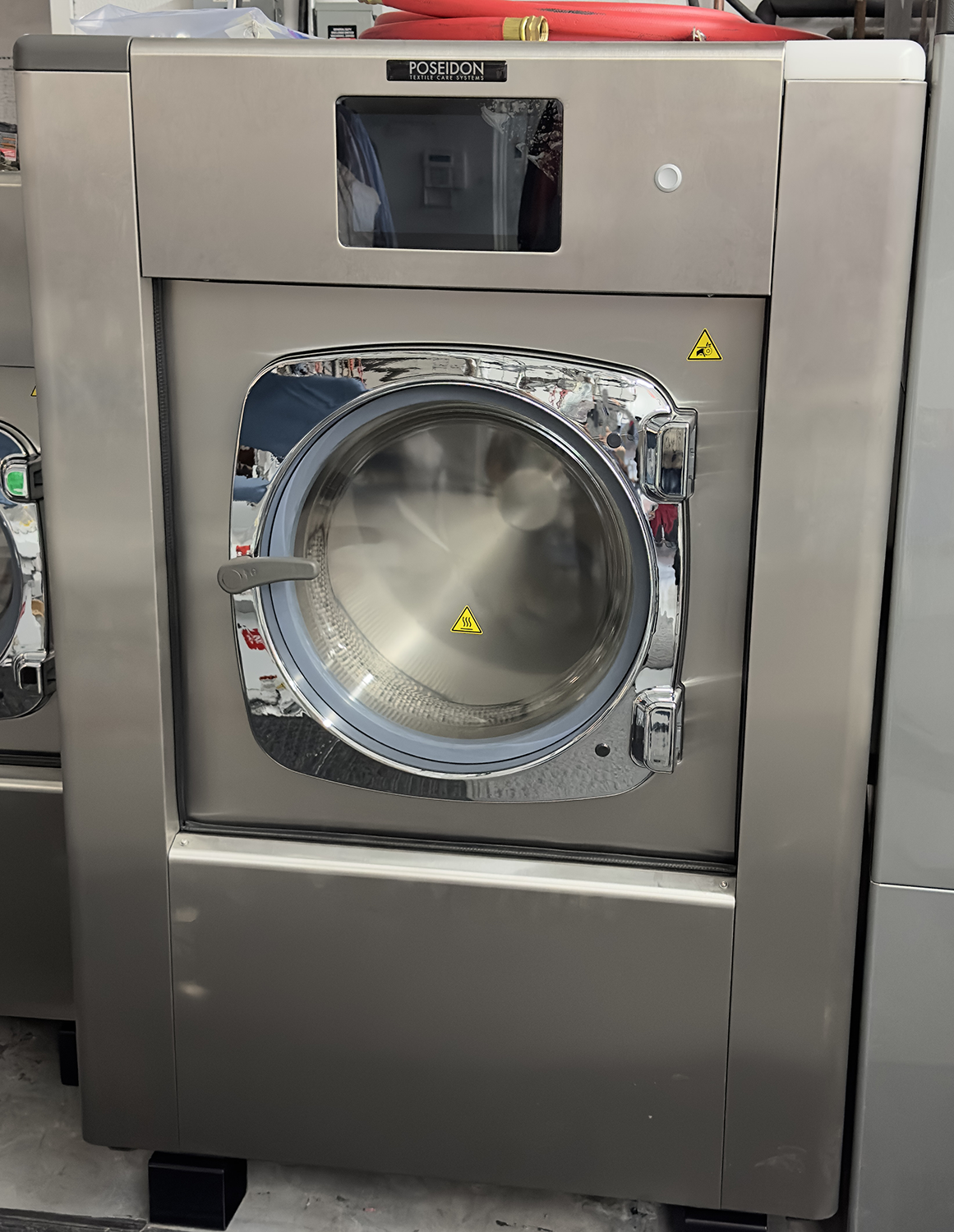 A stainless steel washing machine is sitting on the floor in a laundromat.