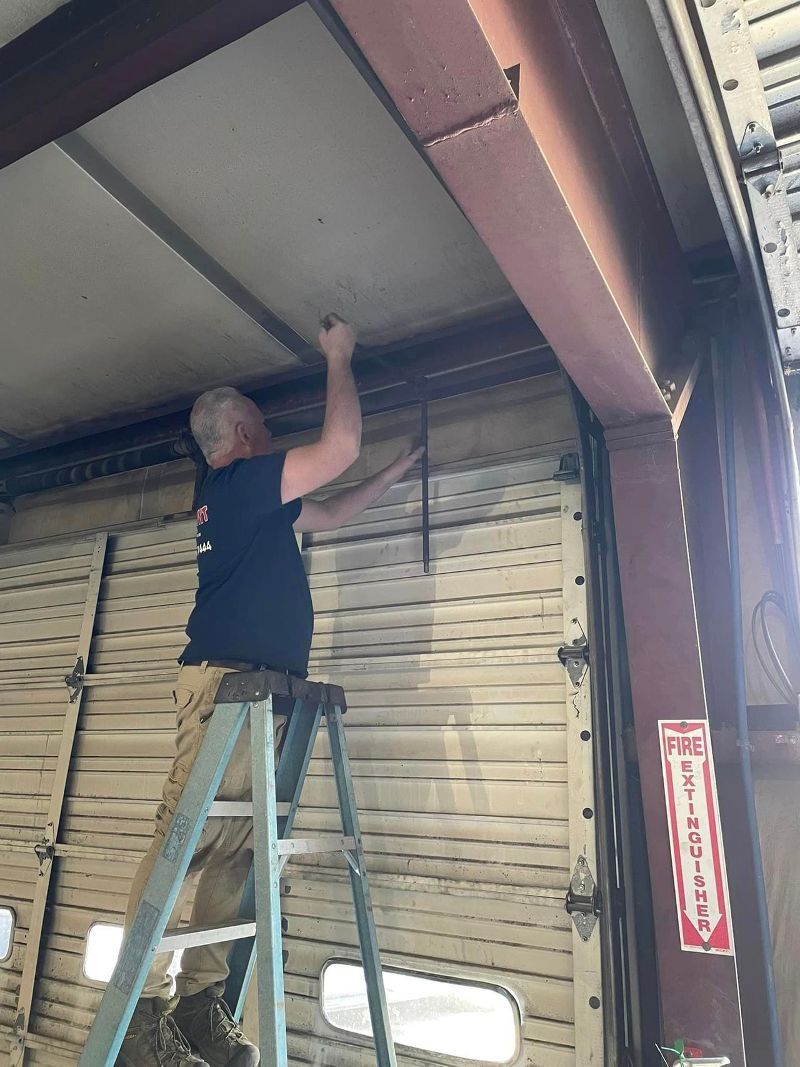 A man is standing on a ladder working on a garage door.