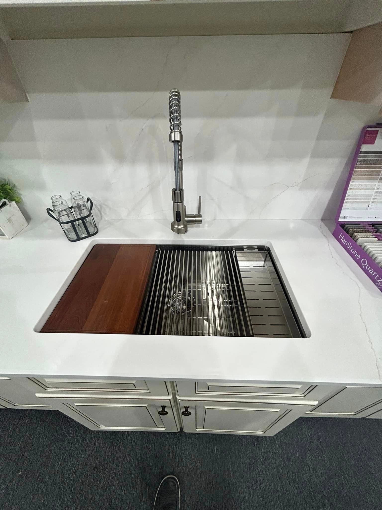 A kitchen sink with a wooden cutting board underneath it.