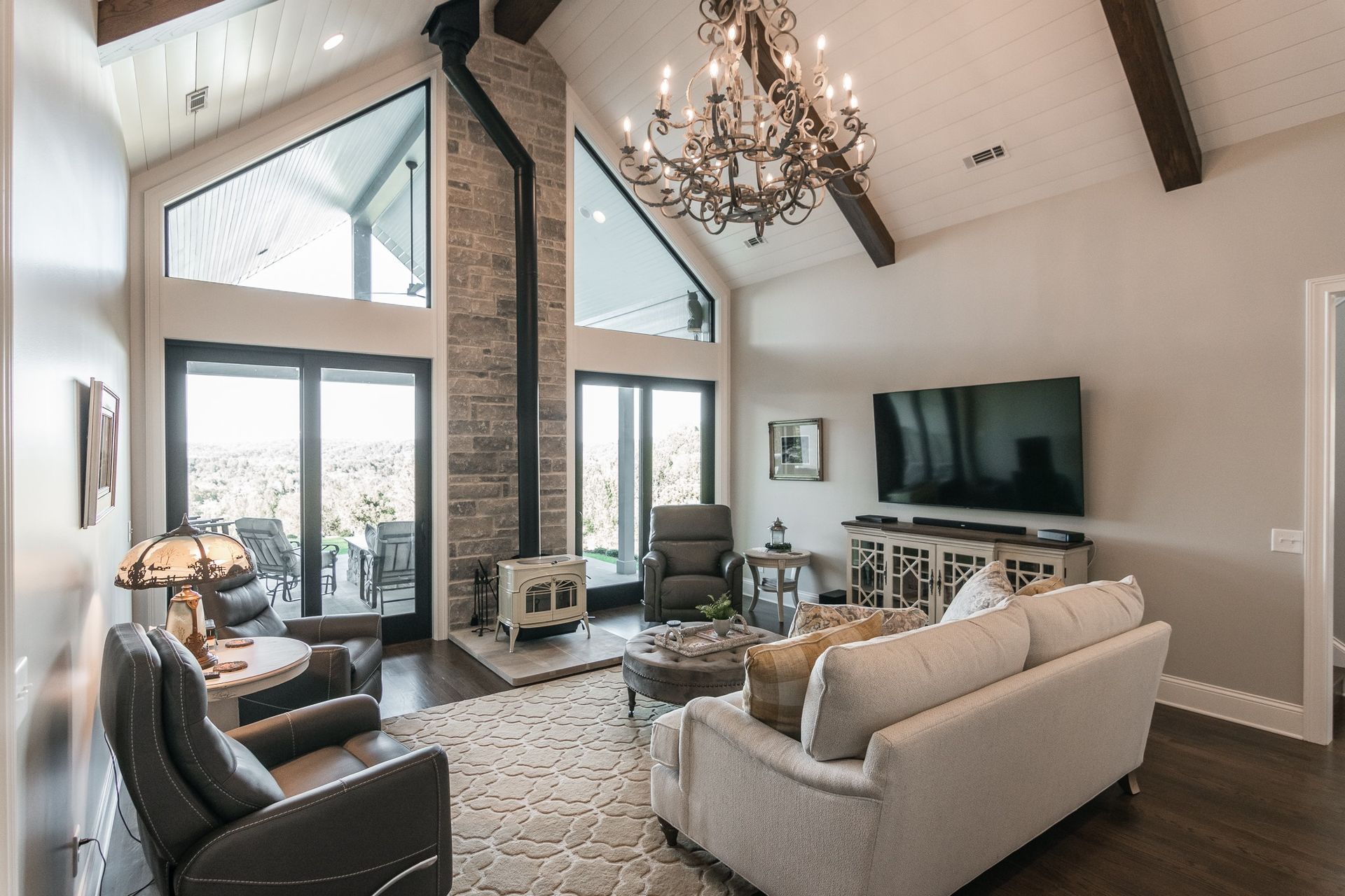 A living room with a couch , chairs , a television and a chandelier.