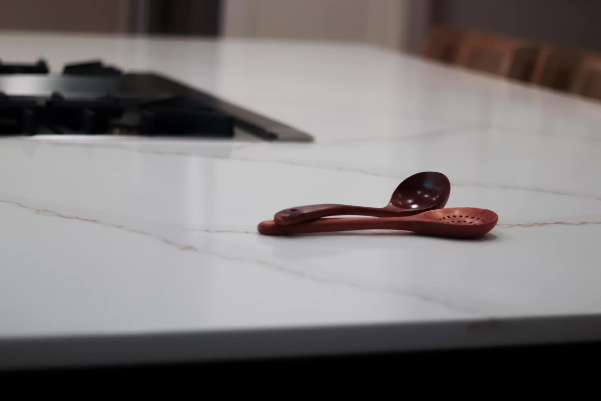 Two wooden spoons are laying on a white counter top.