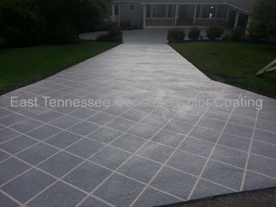 A concrete driveway with a checkered pattern is leading to a house.