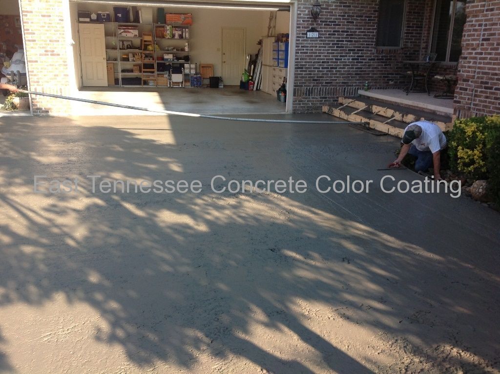 A man is working on a concrete driveway in front of a brick house.