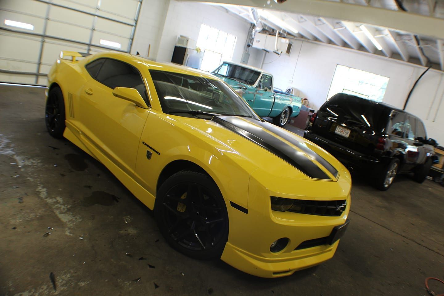 A yellow car with black stripes is parked in a garage
