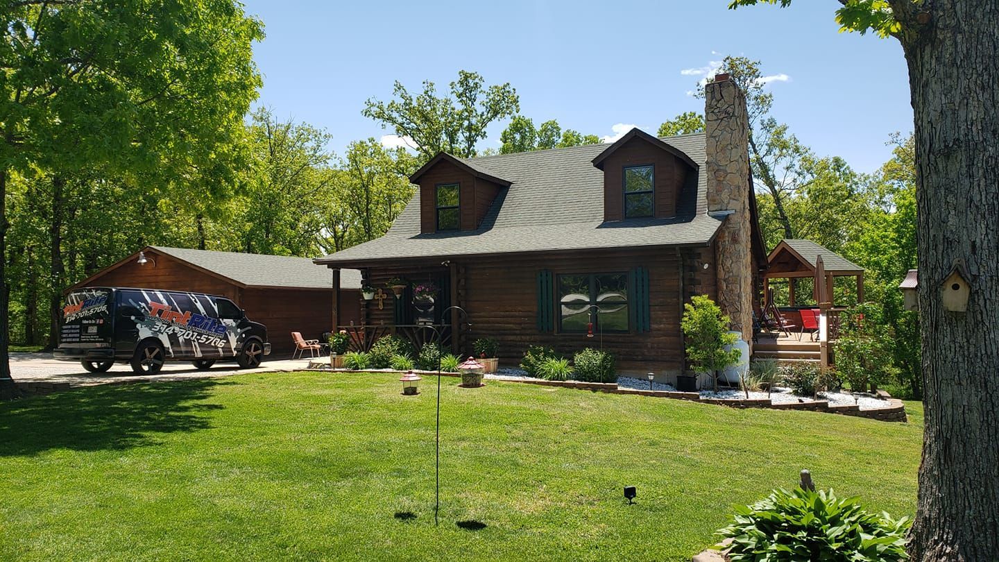 A large log cabin is sitting on top of a lush green hillside surrounded by trees.