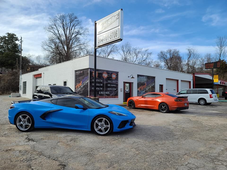 Two sports cars are parked in front of a car dealership.