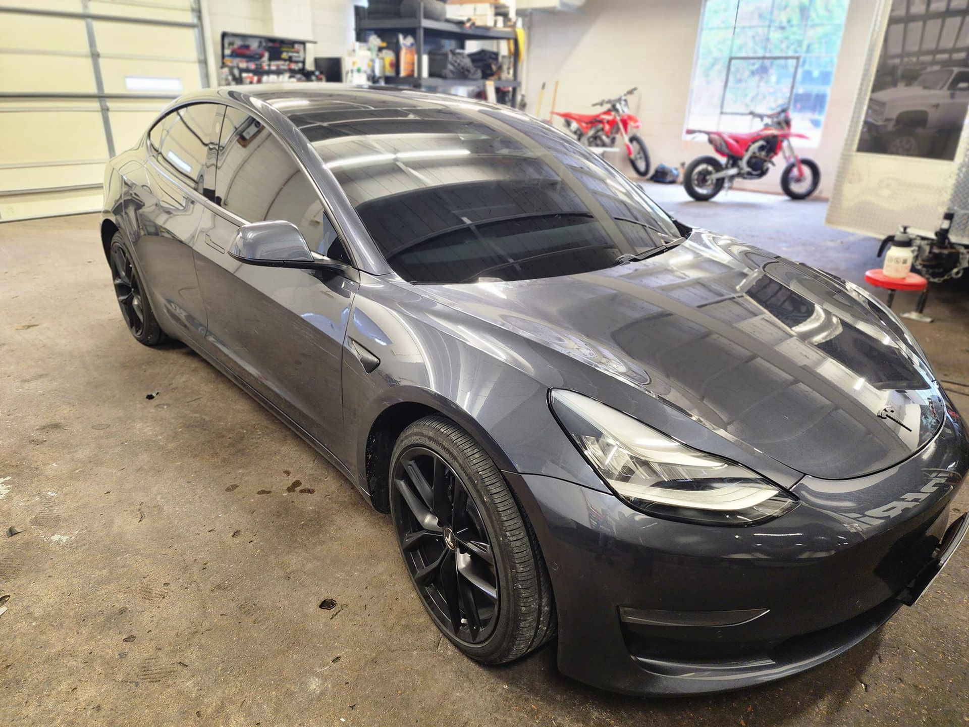 A tesla model 3 is parked in a garage next to a motorcycle.