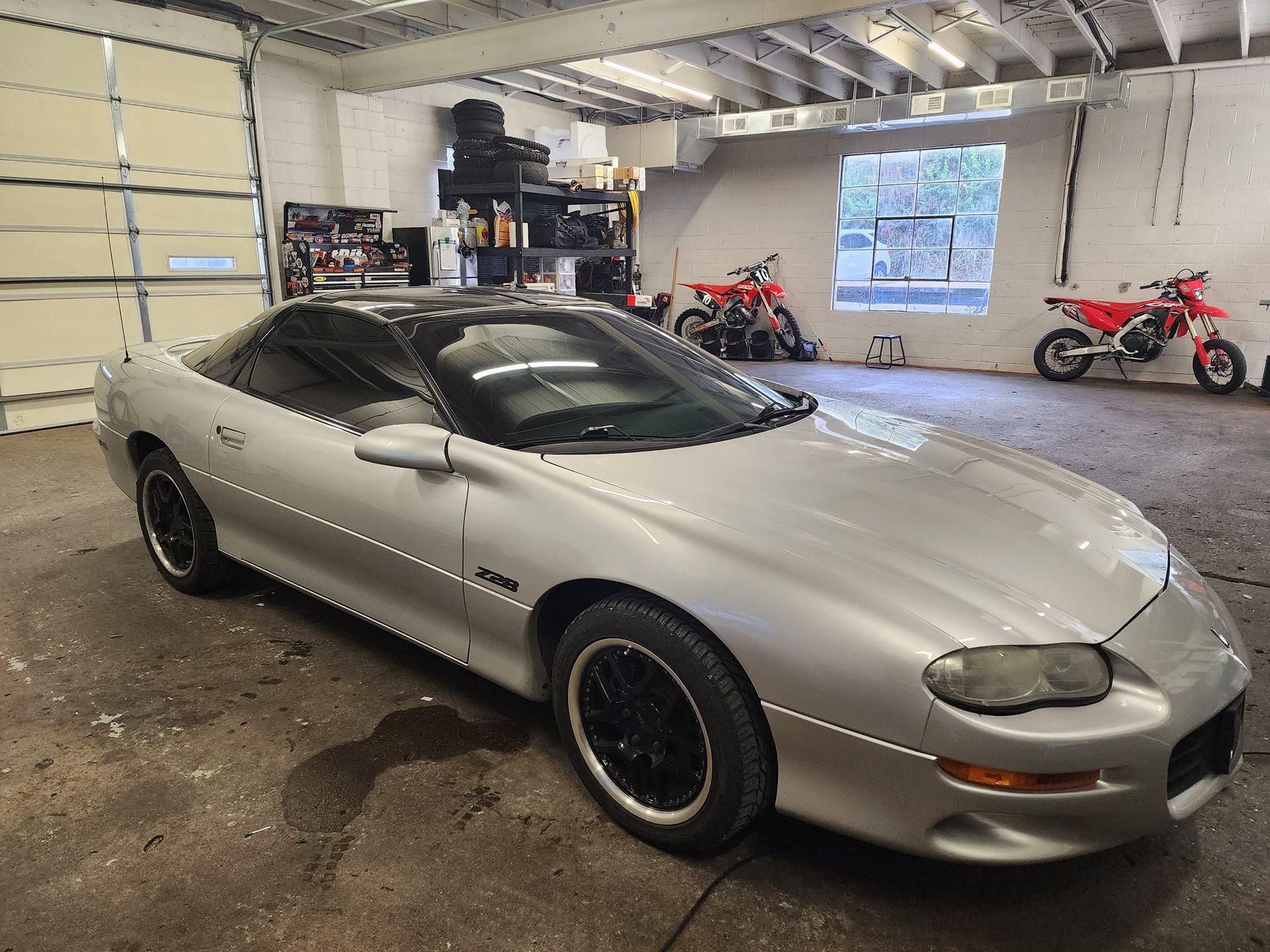 A silver car is parked in a garage next to motorcycles.