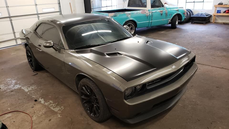 A gray dodge challenger is parked in a garage next to a blue car.