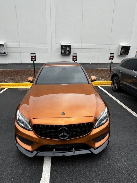 Bronze Mercedes-Benz sedan parked in front of a white building with several air conditioning units.