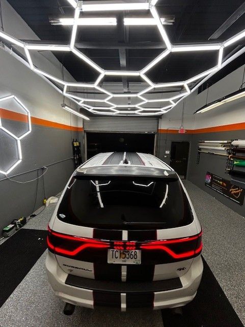 White SUV with black stripes in a garage with hexagon lights.