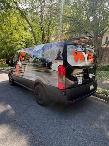 Black van with WYZ logo and vehicle graphic on side, parked on the street.