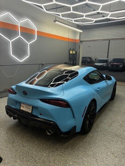 A light blue Toyota Supra sports car in a garage with honeycomb-shaped lights.