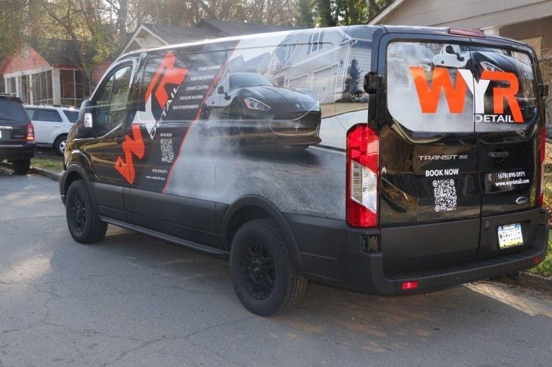 Black van with WYR Detail logo parked on pavement, partial view of houses in background.