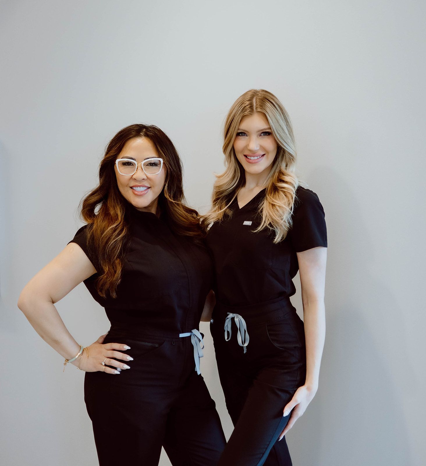 Two women in black scrubs are posing for a picture