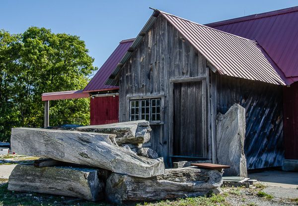 A wooden building with a red roof and a stack of logs in front of it.