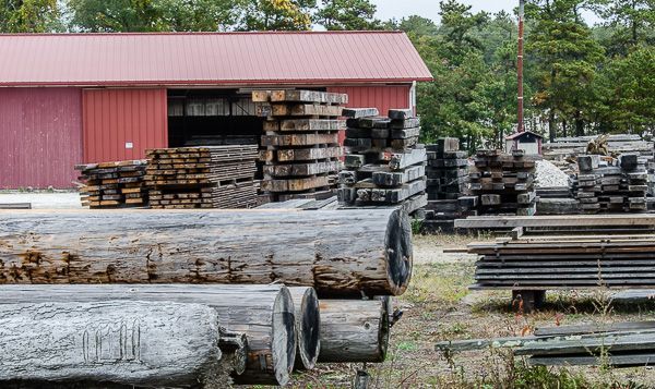 A pile of logs is sitting in front of a red barn.