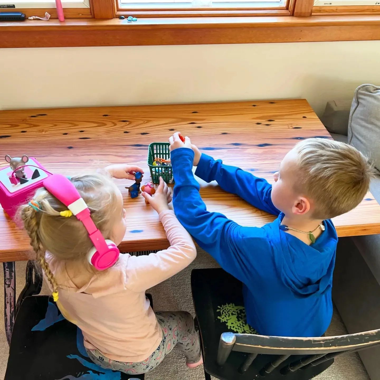 A boy and a girl are playing with toys on a wooden table