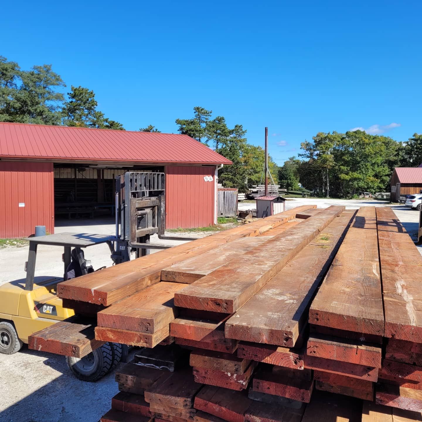 A large stack of wood sits in front of a red barn