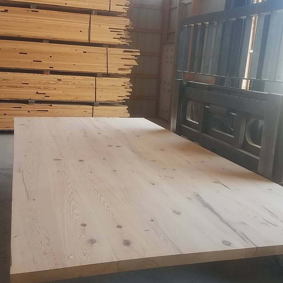 A large piece of wood is sitting in front of a stack of wooden boards.