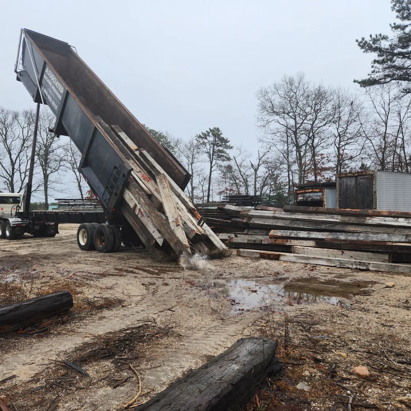 A dump truck is dumping wood into a pile of wood
