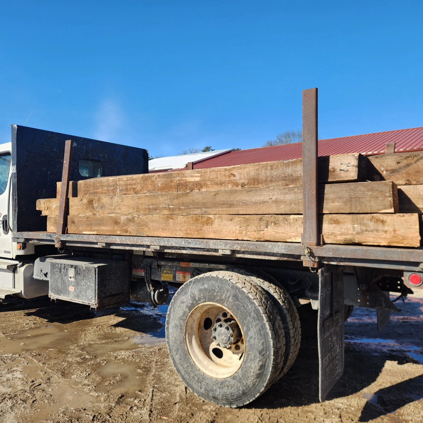 A truck with a wooden bed is parked in the dirt