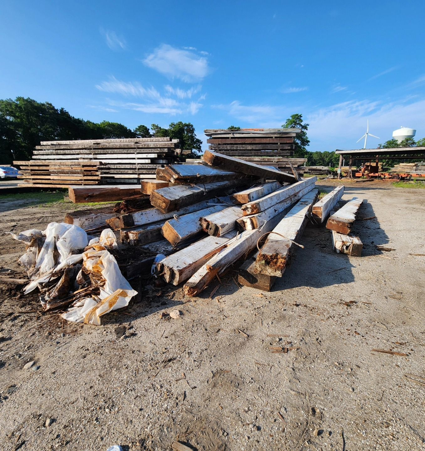 A pile of logs in a dirt field with a water tower in the background