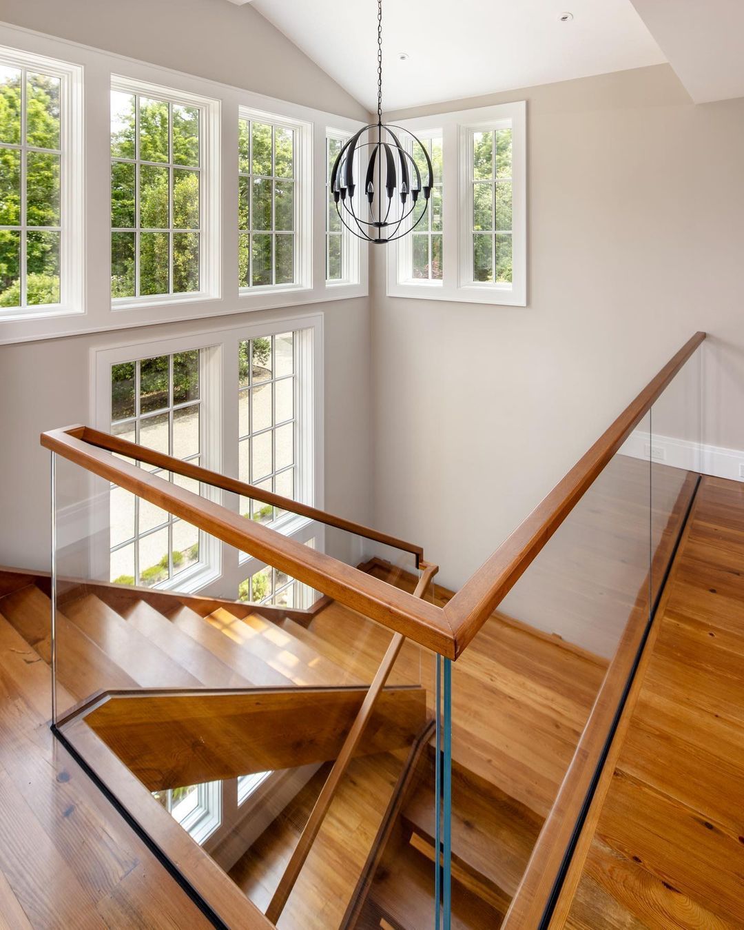 A wooden staircase with a glass railing and lots of windows