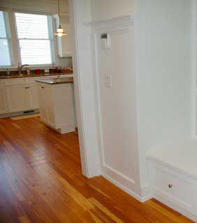 A hallway leading to a kitchen with hardwood floors and white cabinets.