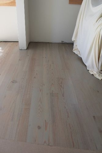A wooden floor in a room with a white blanket on it.