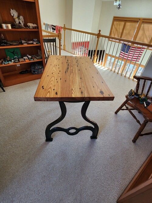 A wooden table with a metal base is sitting in a living room next to a chair.