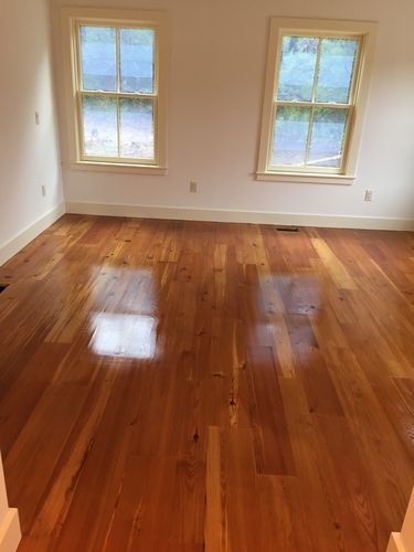 An empty room with hardwood floors and two windows.