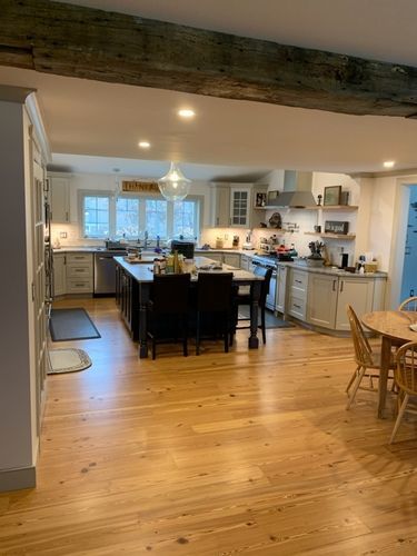 A kitchen with wooden floors , white cabinets , a table and chairs.